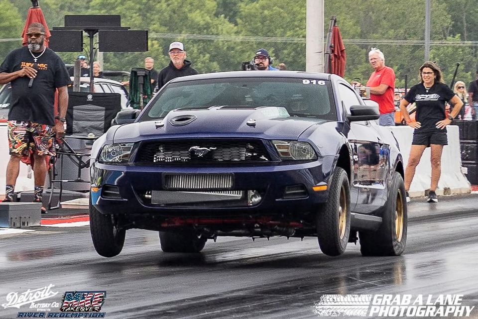 A boosted dark blue Mustang launching hard at the drag strip, front tires in the air