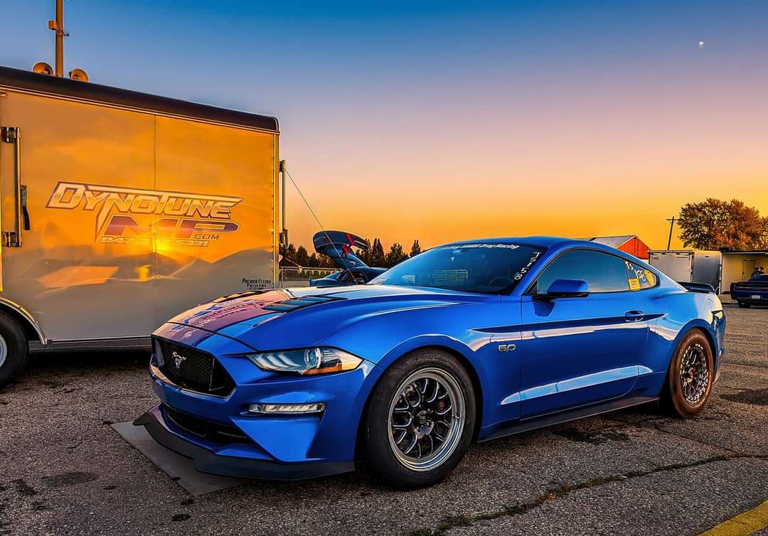 Blue S550 Mustang GT beside the DynotuneMP trailer at sunset